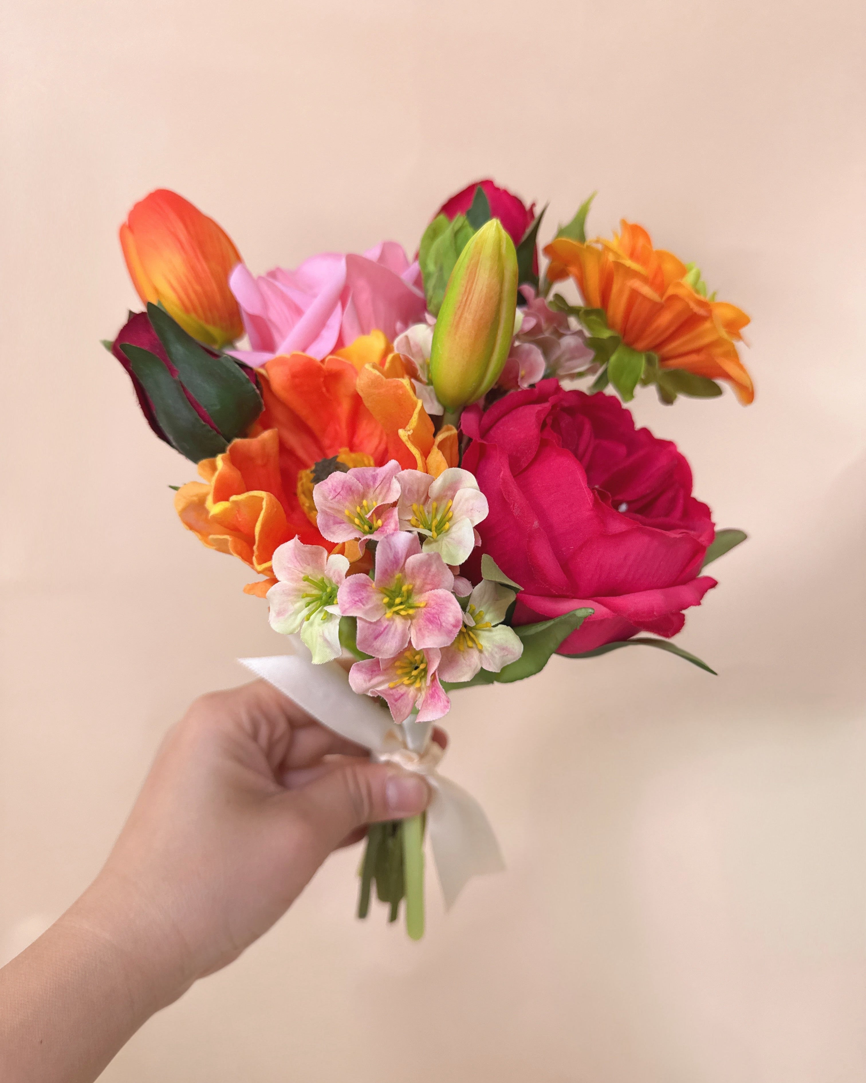 Hand holding a bouquet of colorful flowers against a beige background