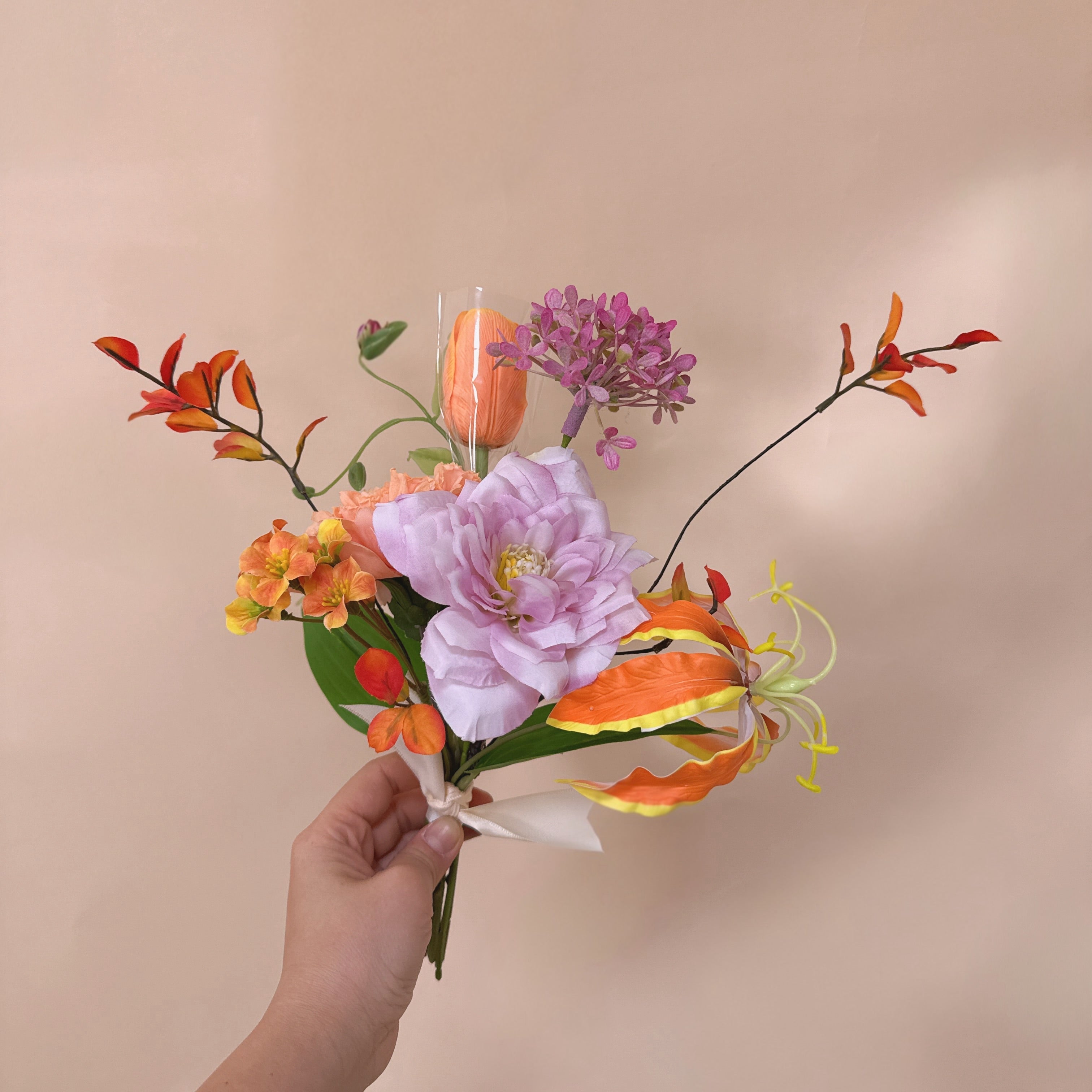 Hand holding a bouquet of colorful flowers against a beige background