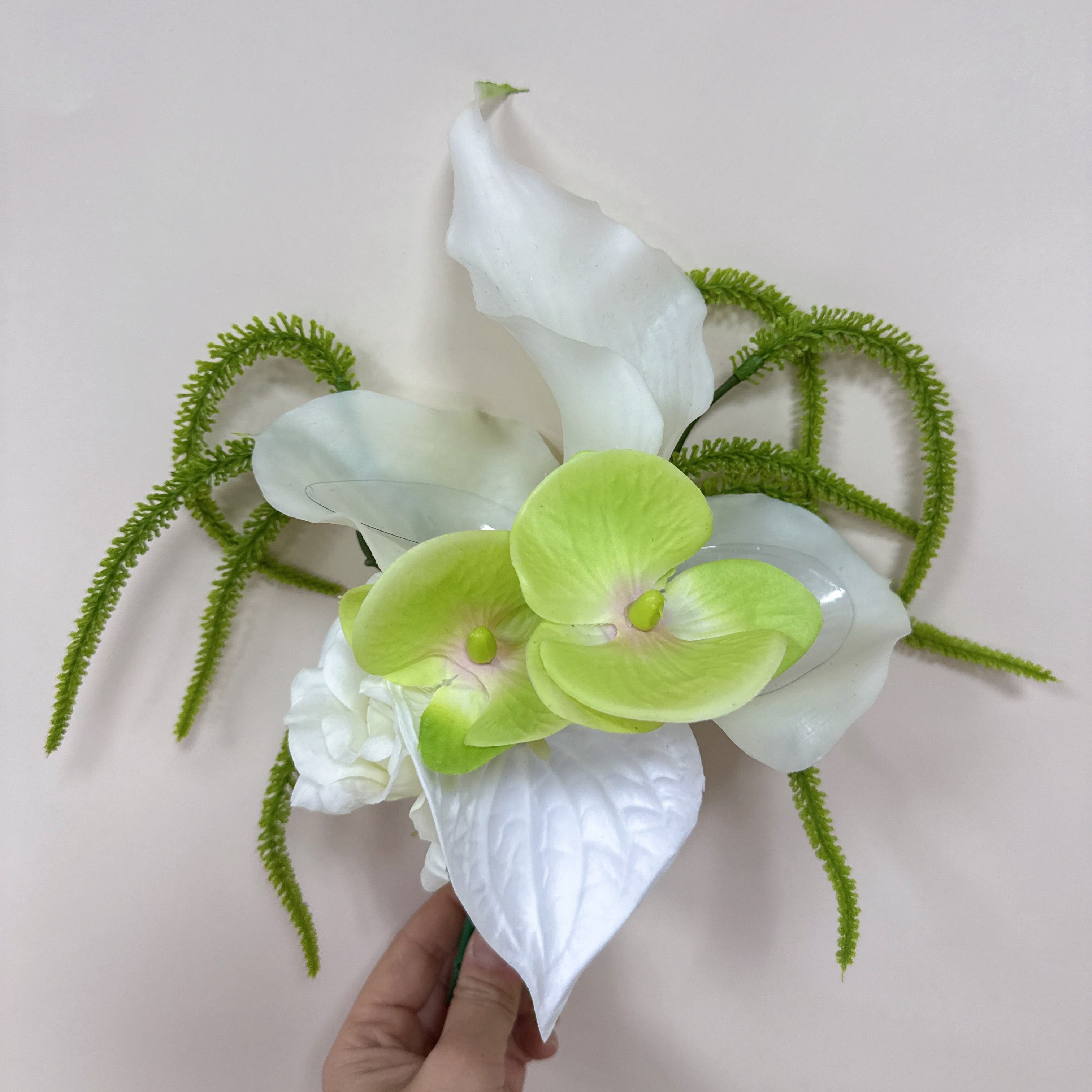 Hand holding a bouquet of white and green flowers against a light background