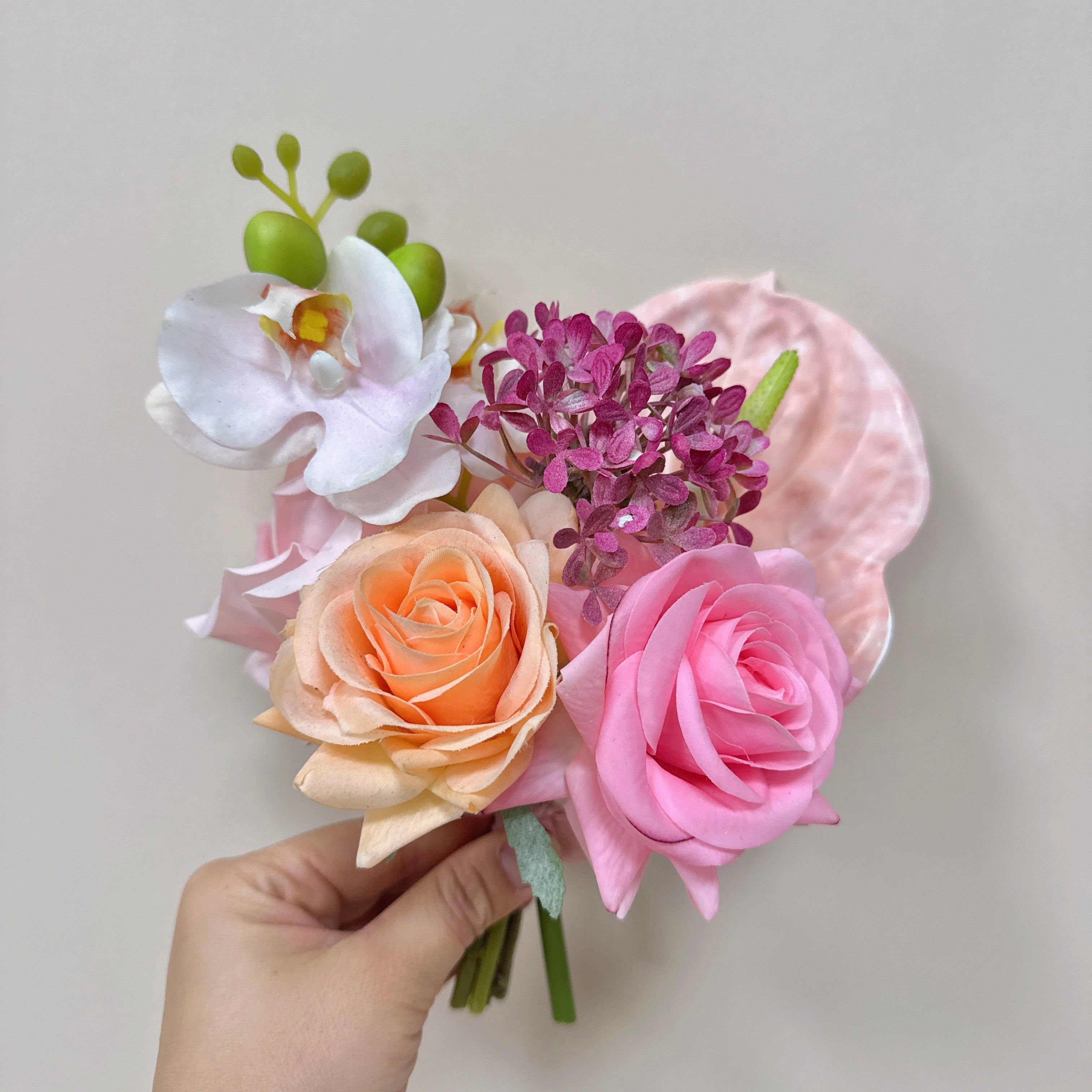 Hand holding a bouquet of artificial flowers against a plain background