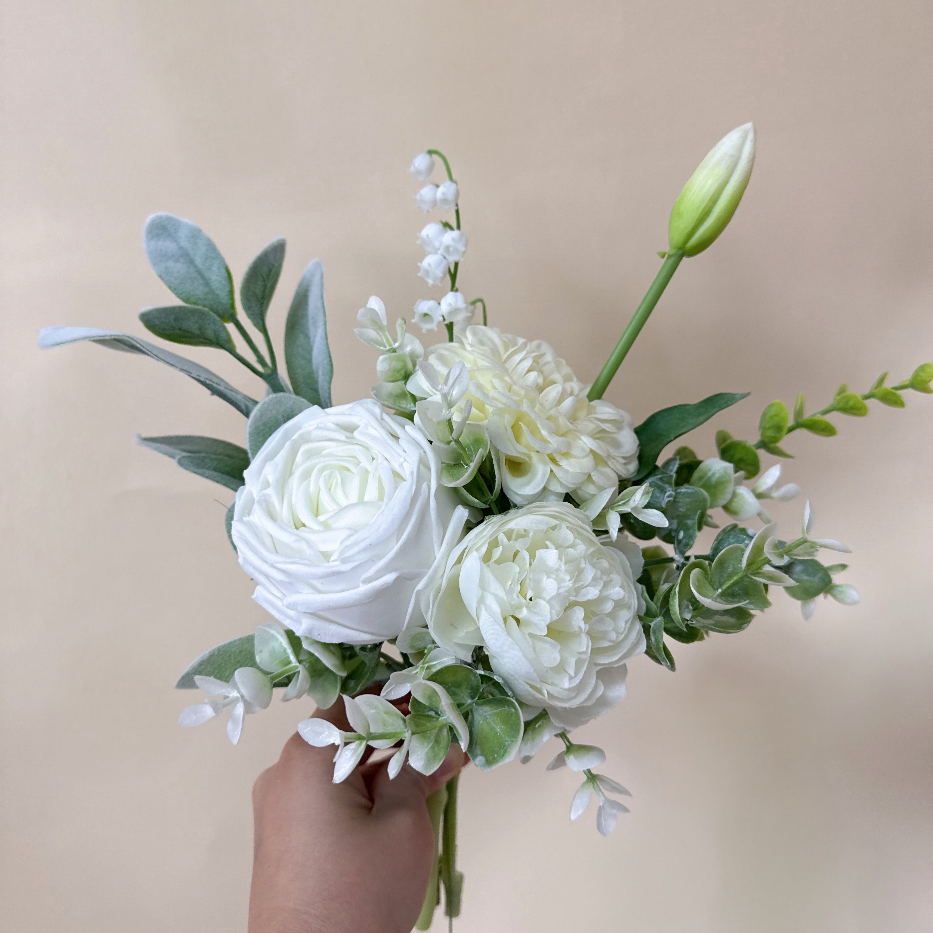 Bouquet of white flowers held by a hand against a beige background