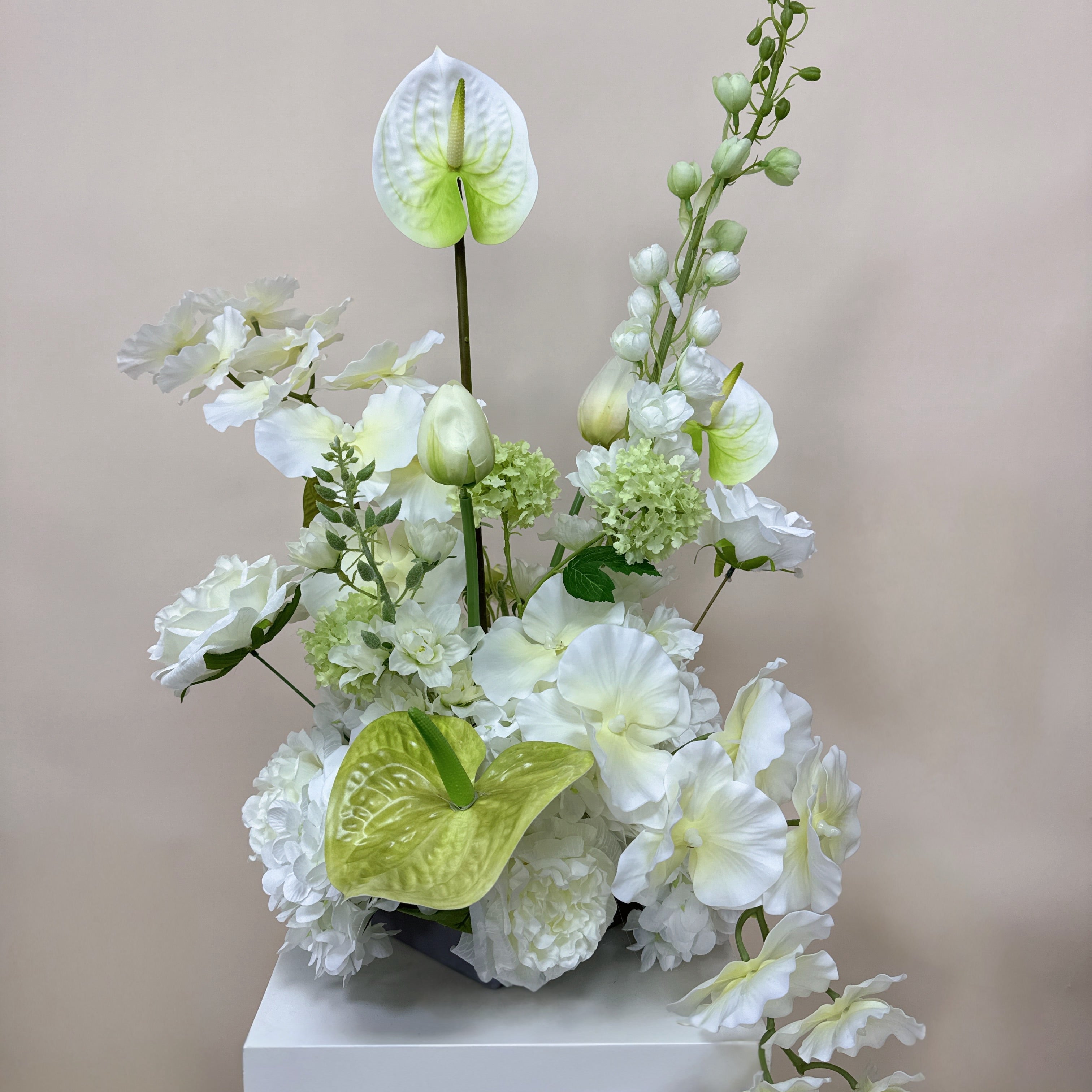 Arrangement of white and green flowers on a white pedestal against a light gray background